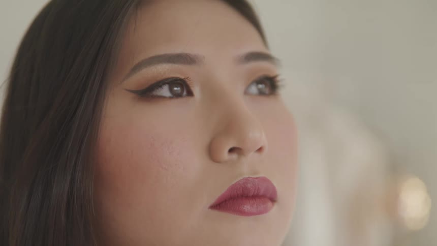 A woman is wearing makeup and standing in a room