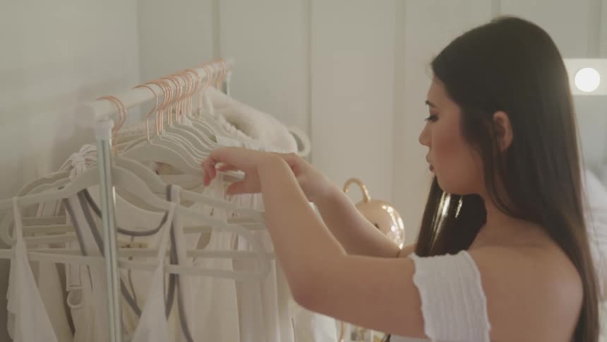 A young asian woman looks through clothing on a clothing rank in a dressing room