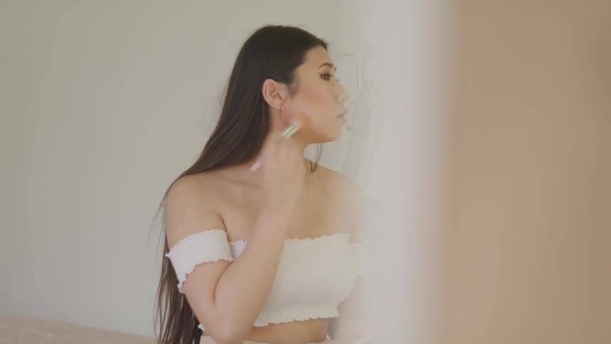 Asian woman with long hair and a white dress puts on makeup in the dressing room