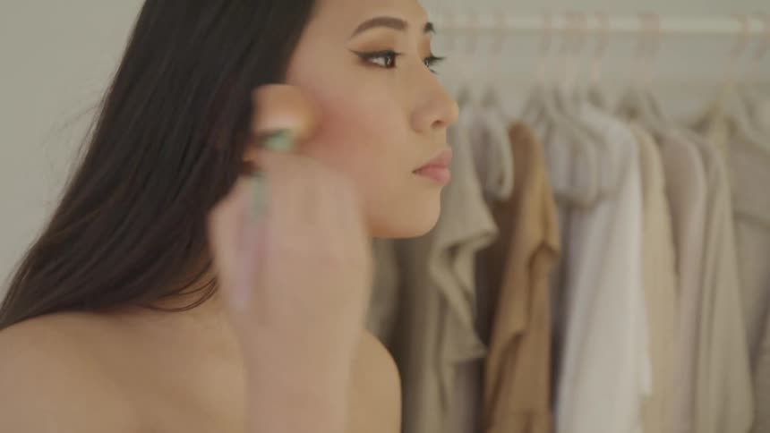 Asian woman with long hair and a white dress puts on makeup in the dressing room
