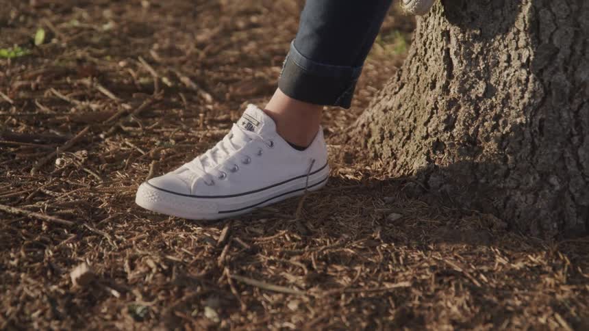 Close up of a females foot on the ground as she leans on a tree with the other foot on the tree