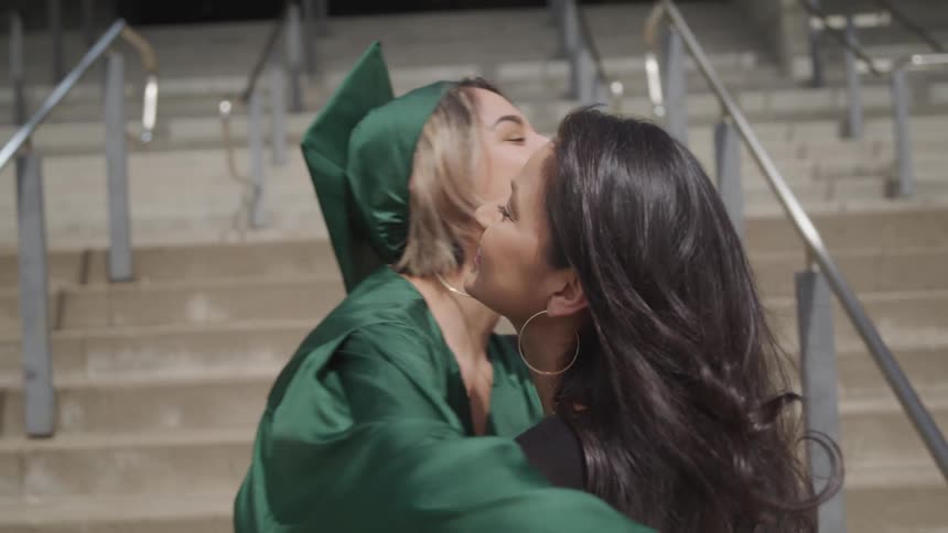 A graduate wearing a cap and gown hugs her mother in front of a set of steps