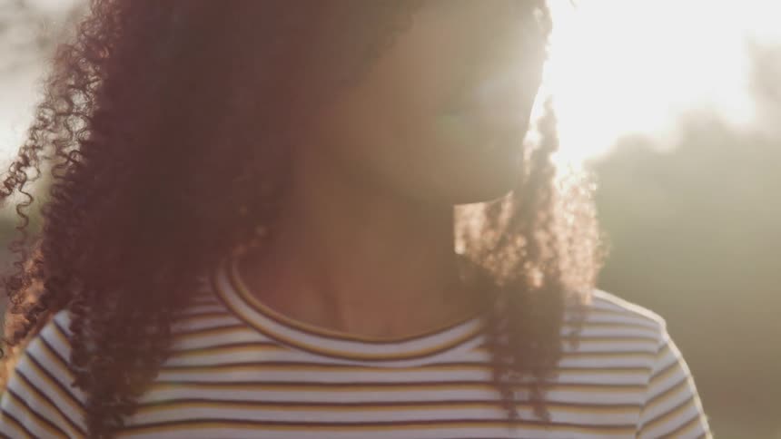 Woman with curly hair stands outdoors under glaring sun