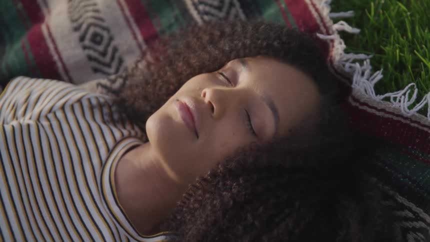 A young woman sleeps on a blanket in a field during the day