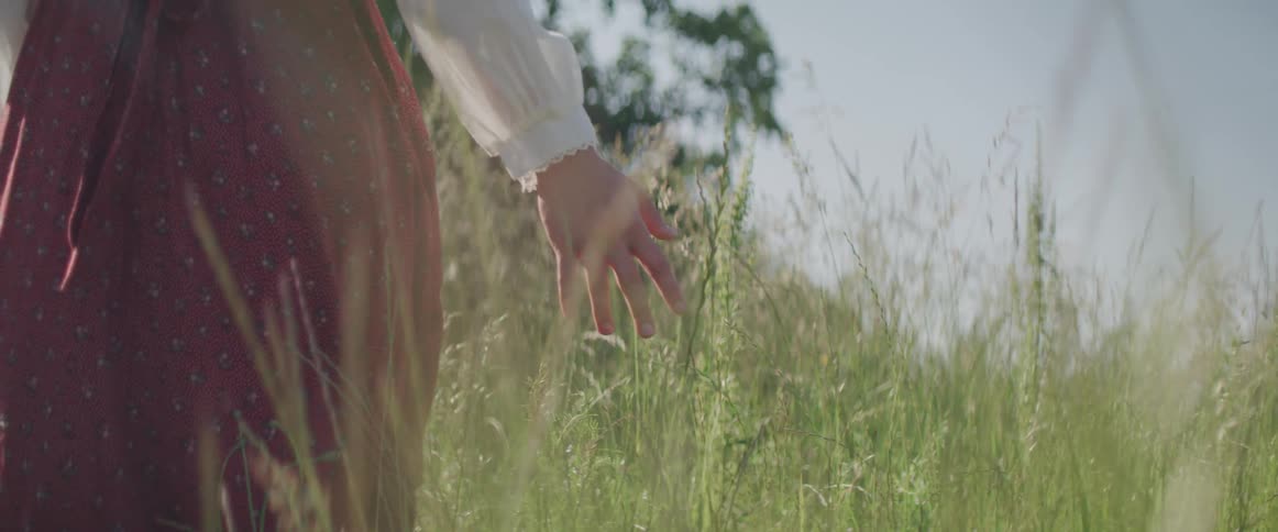 A woman is walking through a field of grass