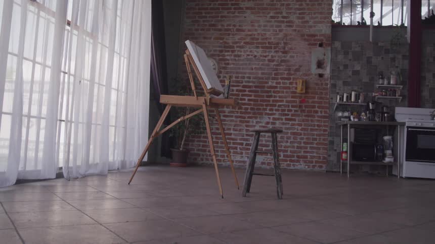 A room with a painting stencil a canvas and a stool next to a window