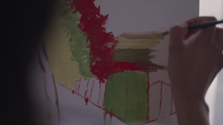 Young woman uses a fine brush to paint on canvas in a room
