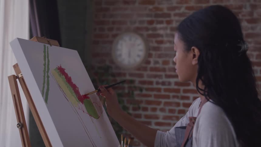 A woman paints on a canvas inside a space with a brick wall