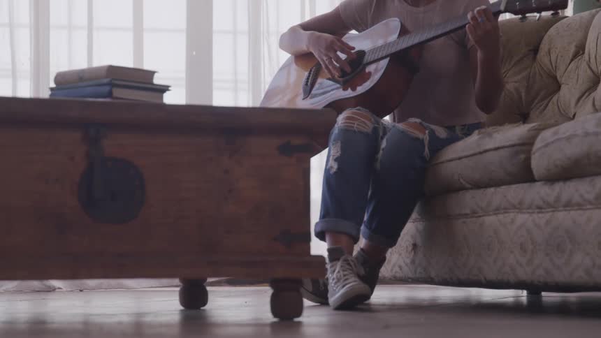 A woman is sitting on a couch and playing guitar