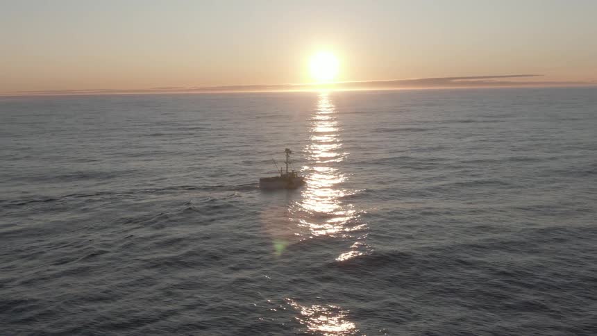 A boat travels through the gentle waves of the open ocean in the evening