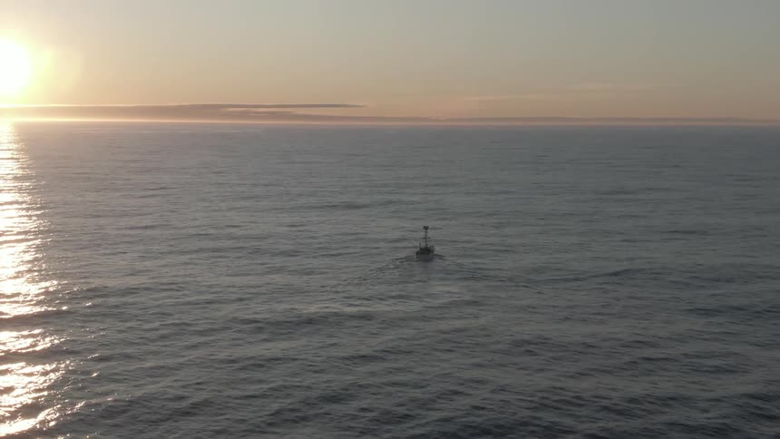 A boat travels across the open ocean in the evening