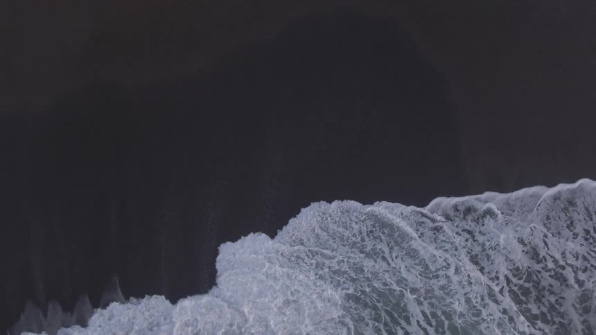 Aerial view of foamy ocean waves break against wet beach sand