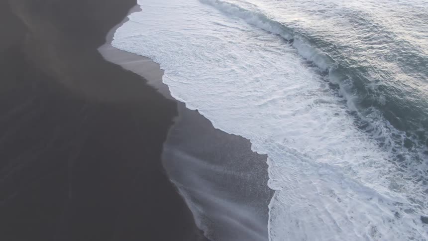 A beach with sand and waves with light reflecting off the water
