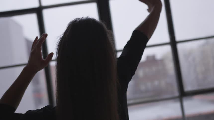 A young woman dancing in front of a window indoors