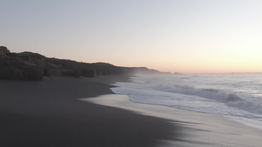 Foamy ocean waves crash againstthe beach at dusk