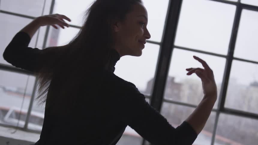 A female dancing in a room with a large window