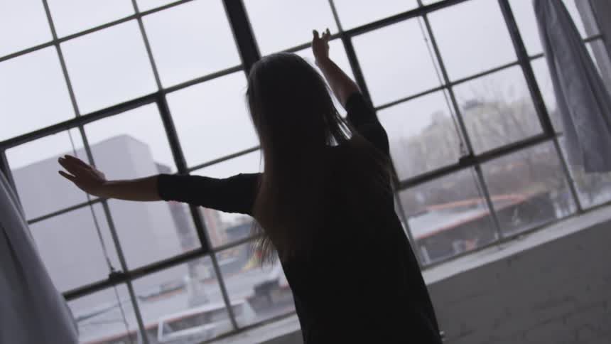 A woman dancing in a room in front of a window with curtains