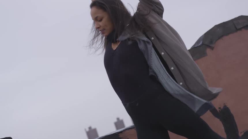 A woman dancing on a rooftop while it is snowing with the sky in the background