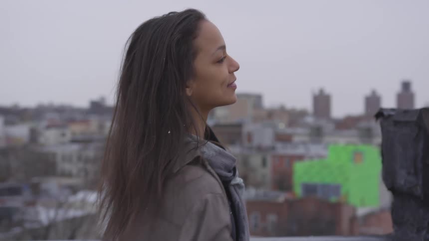 A teenage girl dancing on a rooftop in a downtown area as snow falls