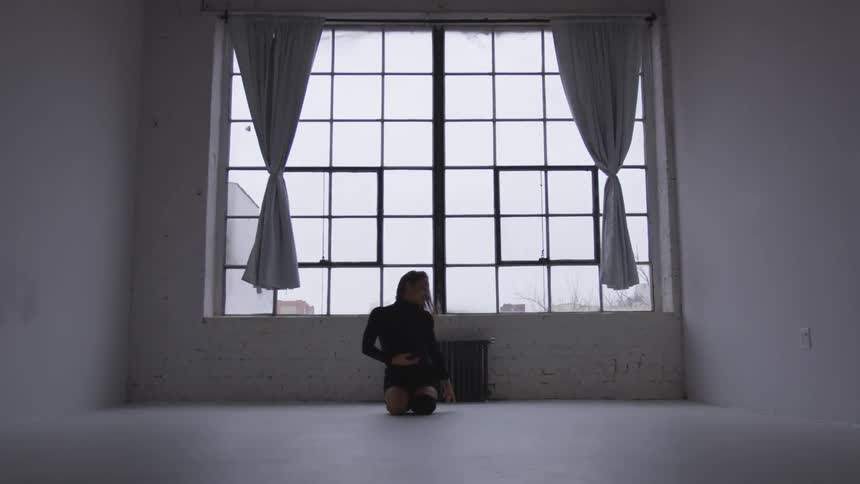A dancer stretches her arms and legs in an open room studio