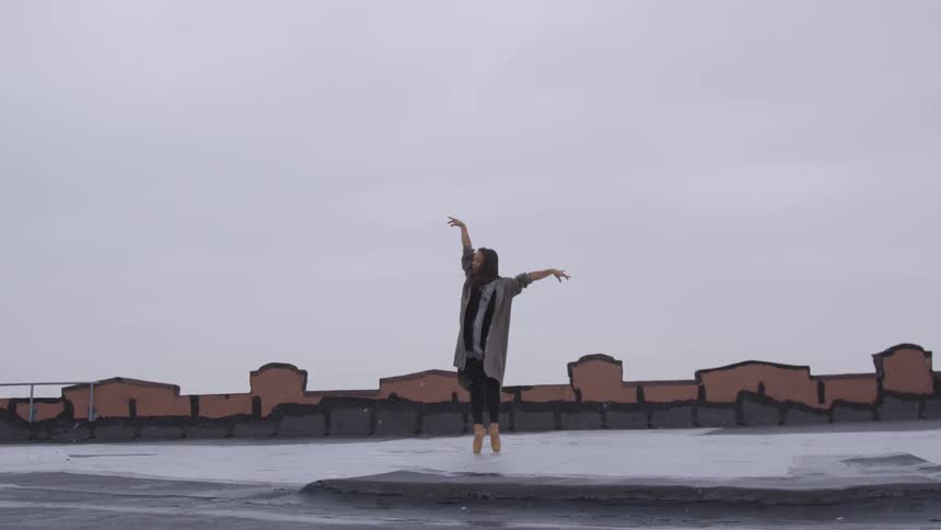 A teenage girl dances on a roof top in the snow