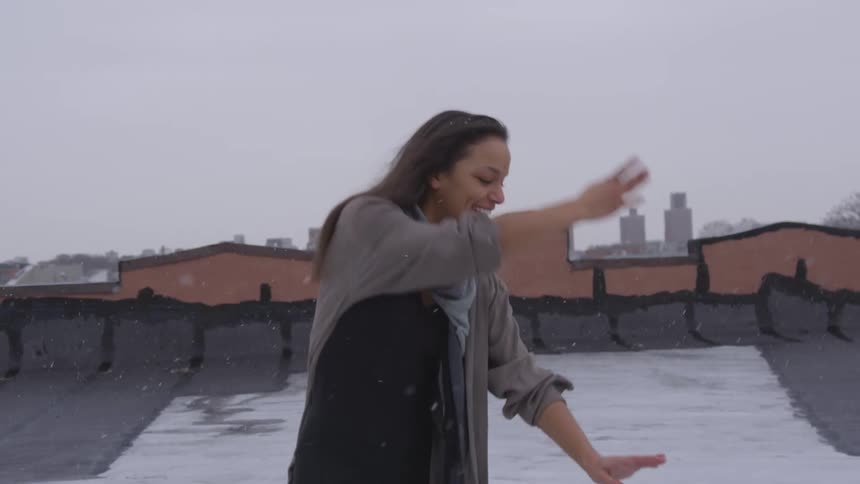 A woman is dancing on a rooftop in a downtown city during winter