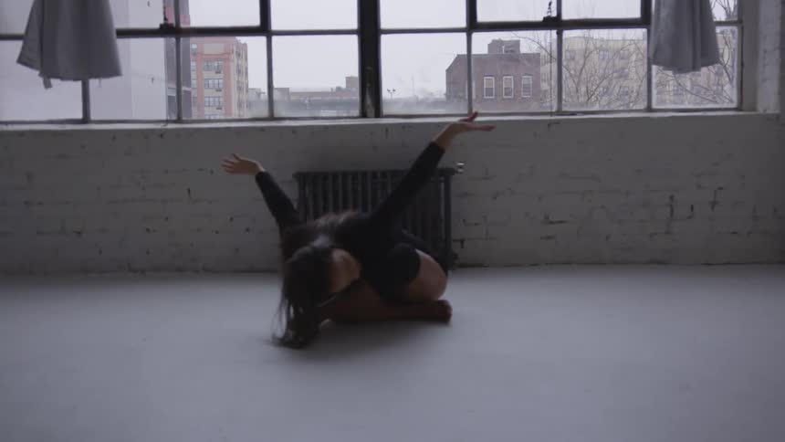 A woman sitting on the floor stretching with a window and curtains in the background
