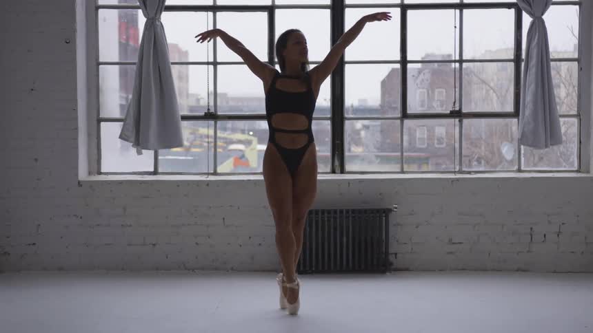 Woman in leotard ballet dancing in front of large window