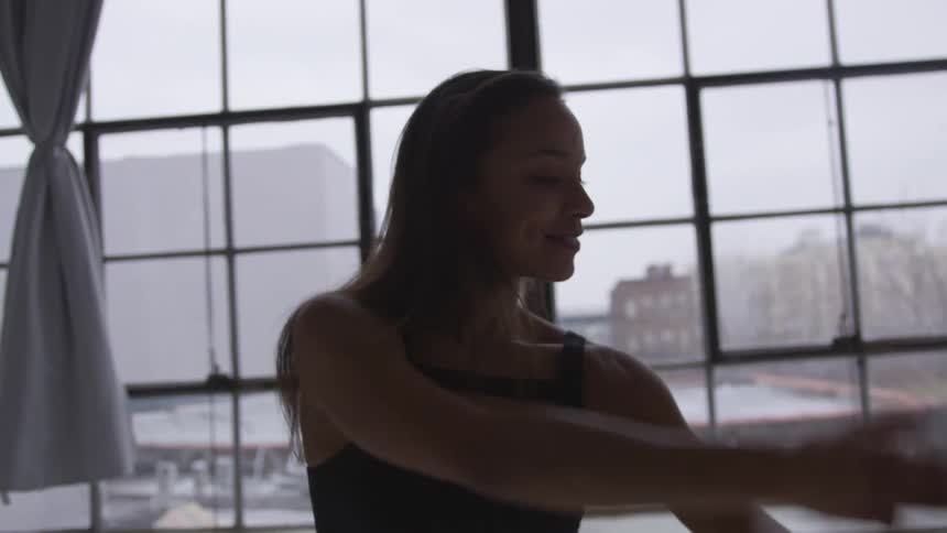 A woman is dancing indoors next to a window