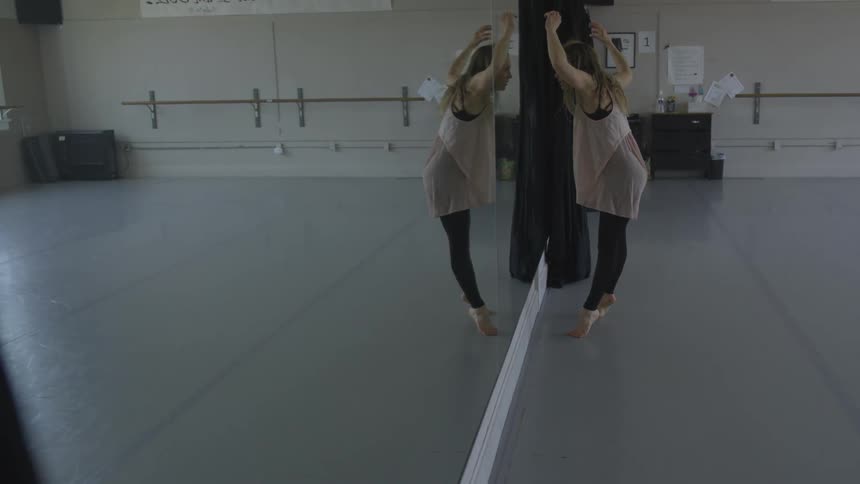 A female caucasian dancing in front of a mirror in a dance studio
