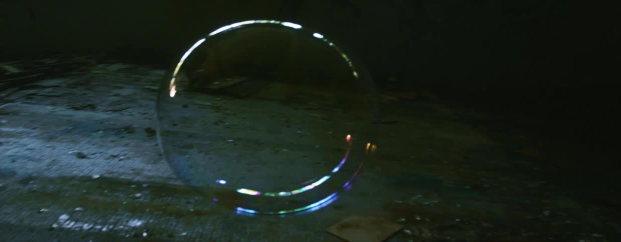 A large bubble pops while floating in the dark