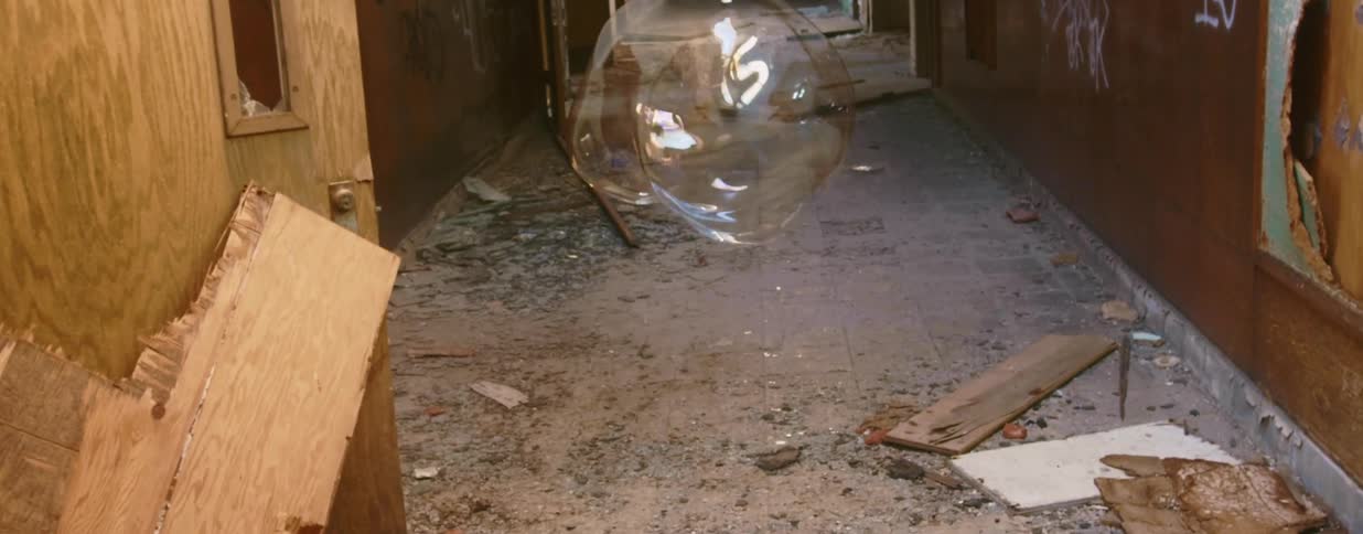 A large bubble floating down the hallway of an abandoned and graffitied building