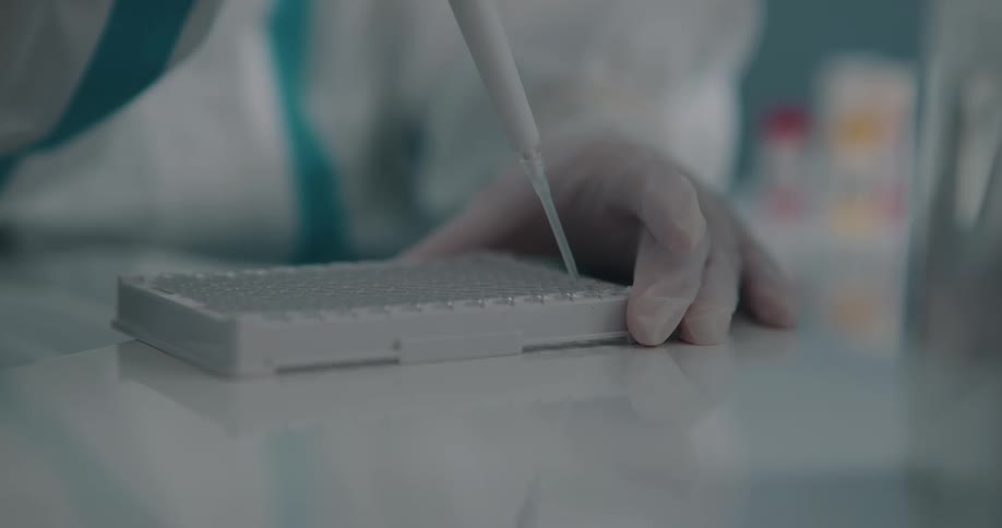 A person in a lab places droplets of medication from a syringe in to a tray