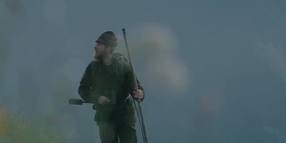 Man carrying a walking stick and a microphone walks outdoors with a dog