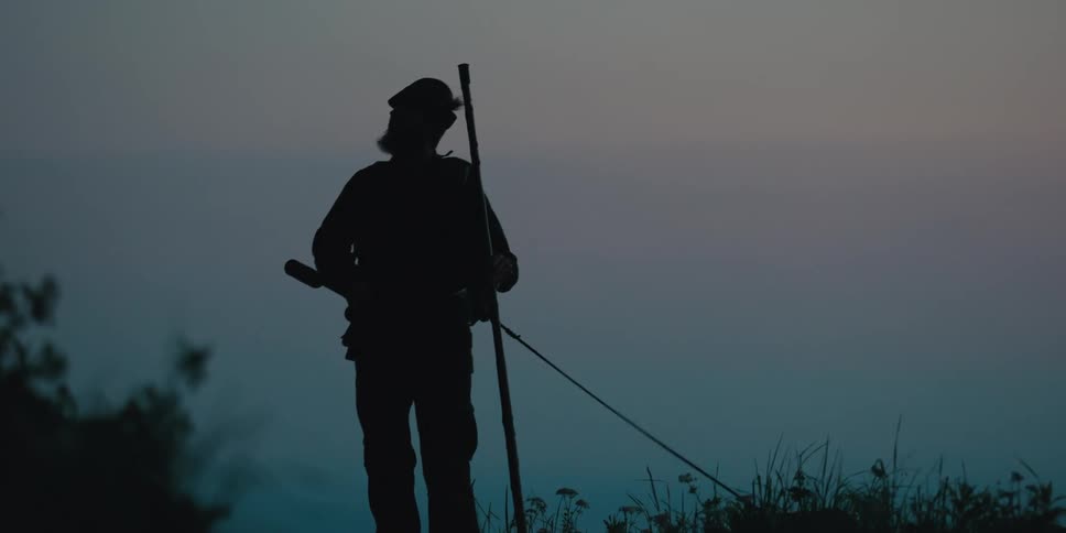 Silhouette of a hunter carrying a rifle walking outdoors with his dog