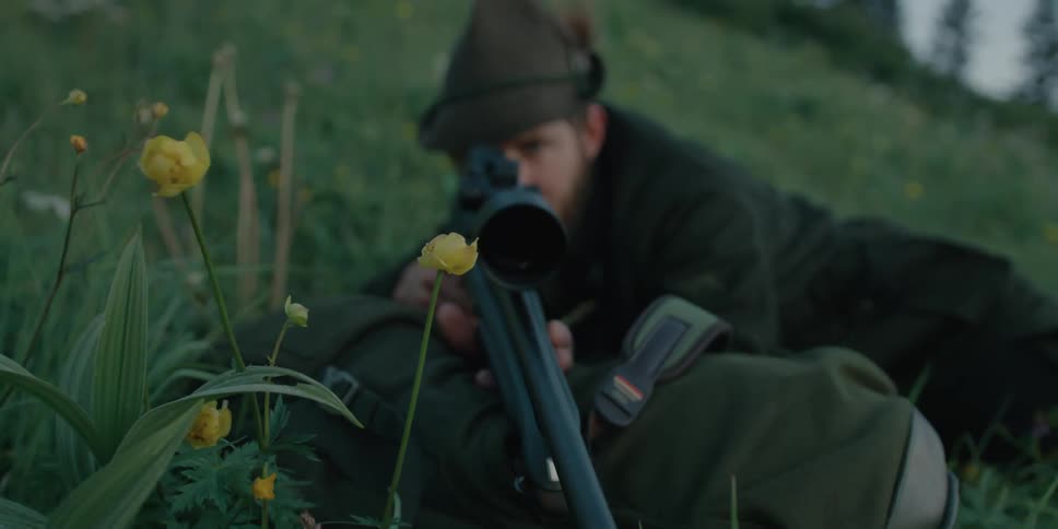 A man looks through the scope of a rifle as he lies in a field