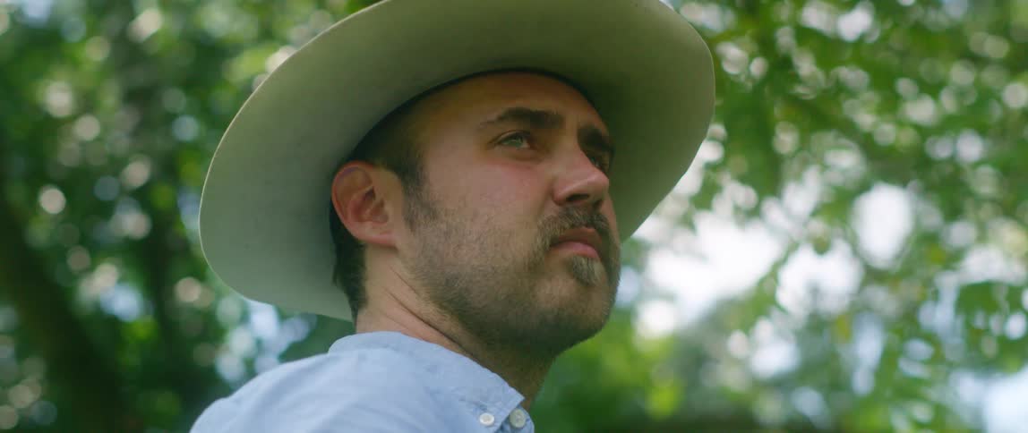 Man wearing white cowboy hat standing under trees