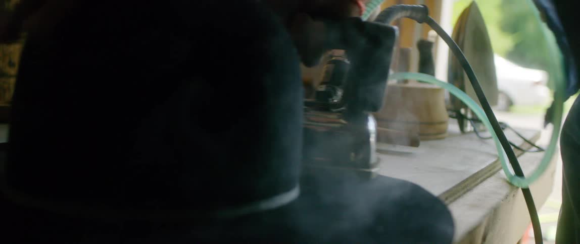 Person ironing brim of hat on workbench