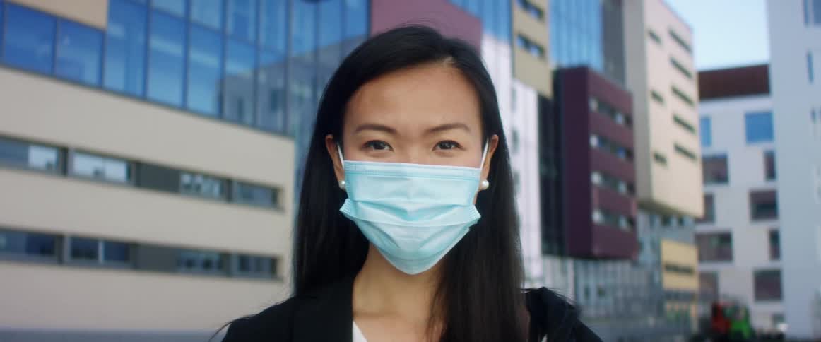 Asian woman with long straight hair and a blue mask faces the camera with eye contact
