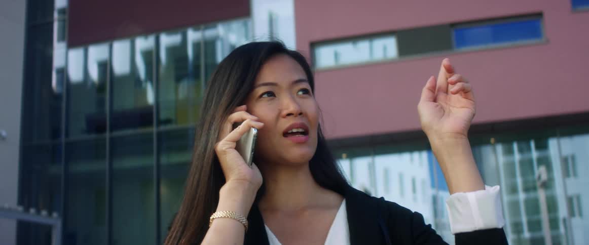 Asian woman with with long hair talks on the phone in front of a high rise building