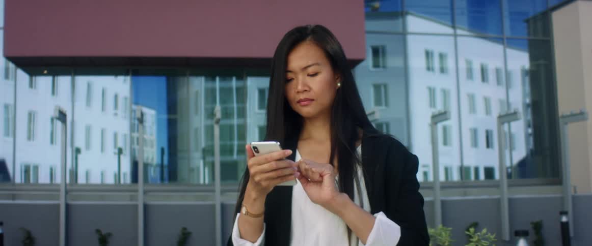 A woman stands outside of an office building and scrolls on her phone