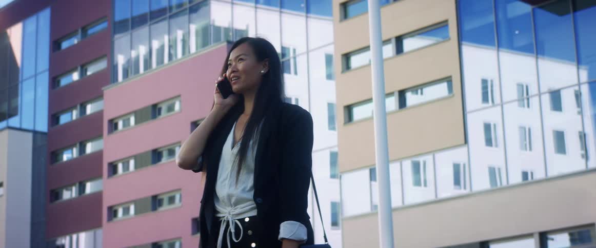 Woman smiles and talks on a cell phone while standing near the city buildings