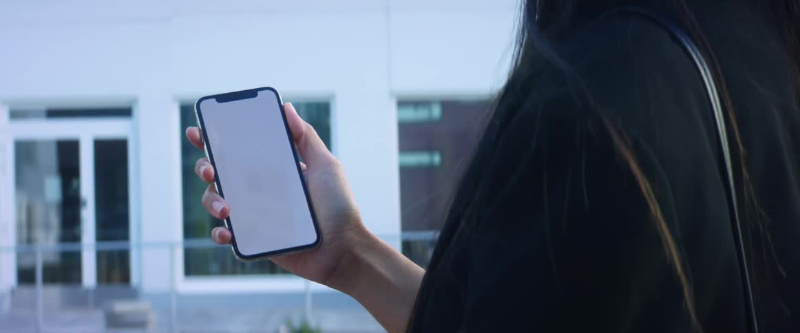 A woman uses her smart phone while standing outside in front of a building