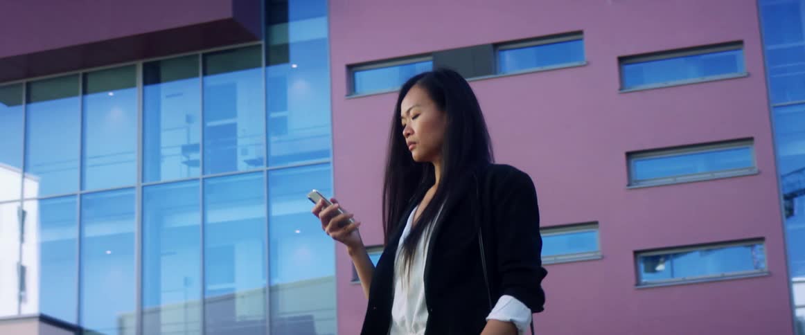 A woman is texting on a cellphone and walking through a city