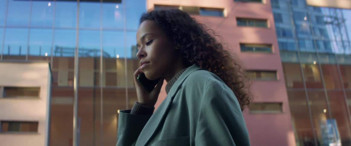A woman is walking through a downtown city and talking on a cell phone
