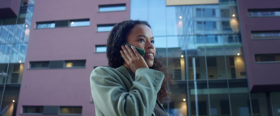 A young woman standing outside an office building talks on her cell phone