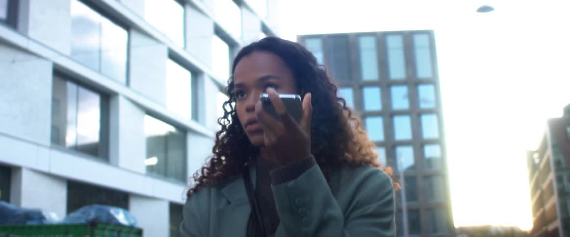 A woman stands outside of a city building talking on a cell phone