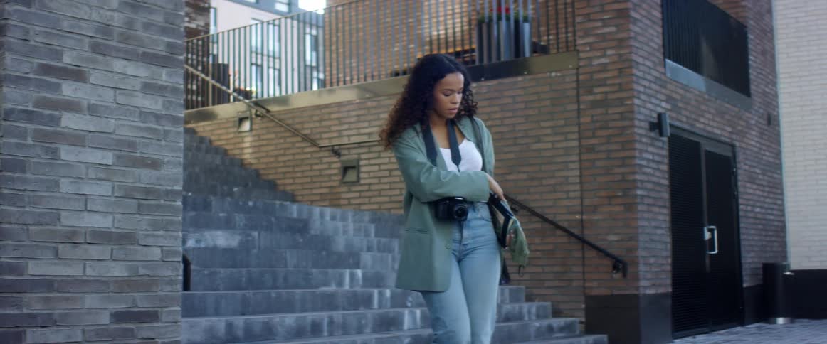 A woman walks down an exterior building staircase and puts on a face mask