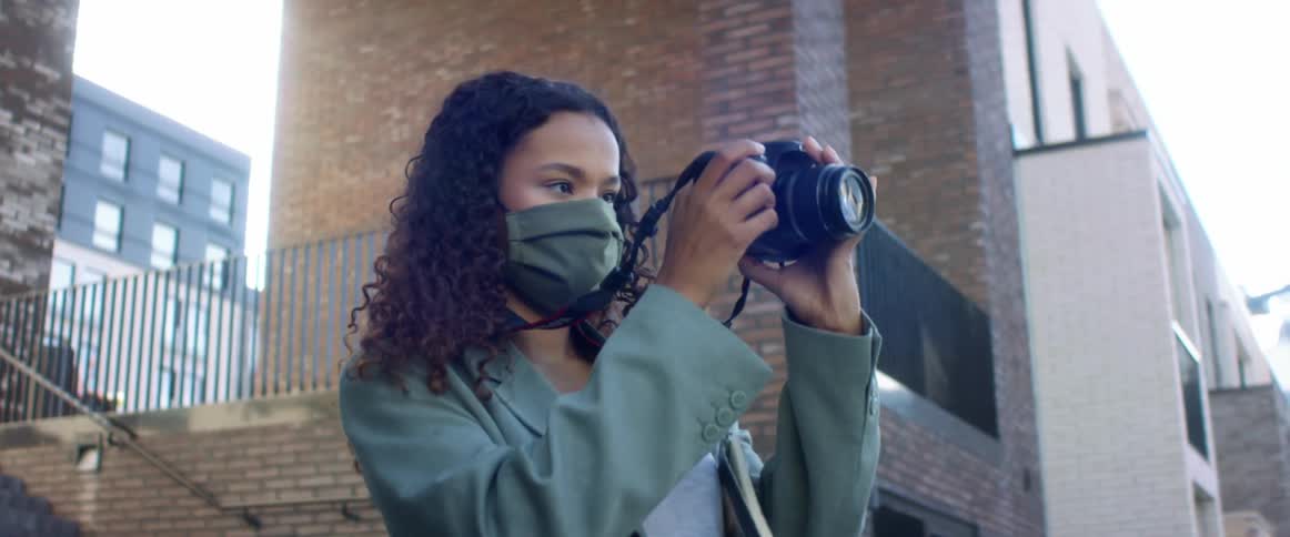 A teenage girl standing outside an apartment building looks through a camera lens