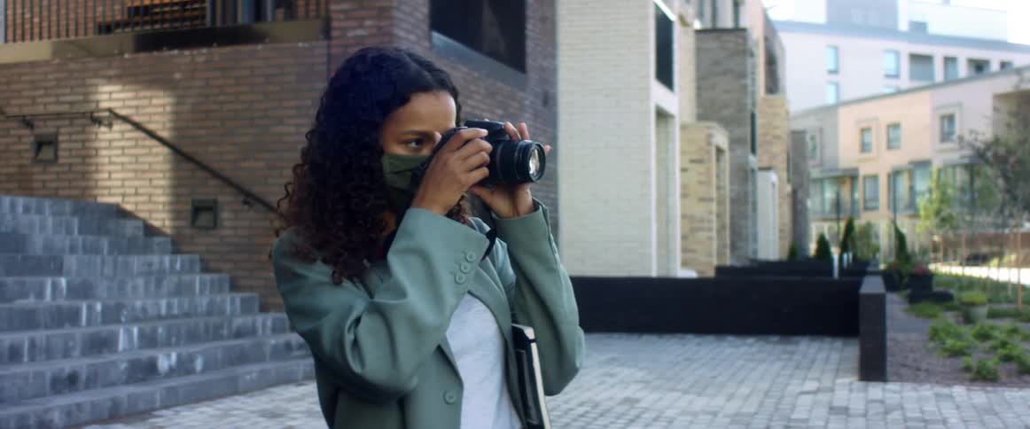 A woman stands outside a city building and uses a professional camera to take a picture